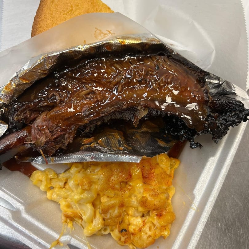 Tasha's soul food meal with saucy ribs, mac and cheese, and cornbread in a takeout container.