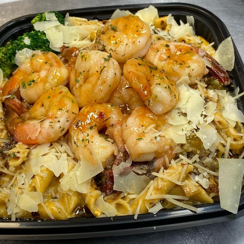 Shrimp pasta with broccoli and parmesan cheese in a black takeout container from Tasha's.
