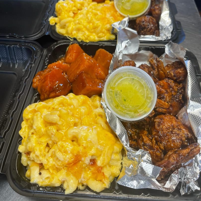 Two takeout containers of Tasha's soul food, with mac and cheese, candied yams, and BBQ chicken.