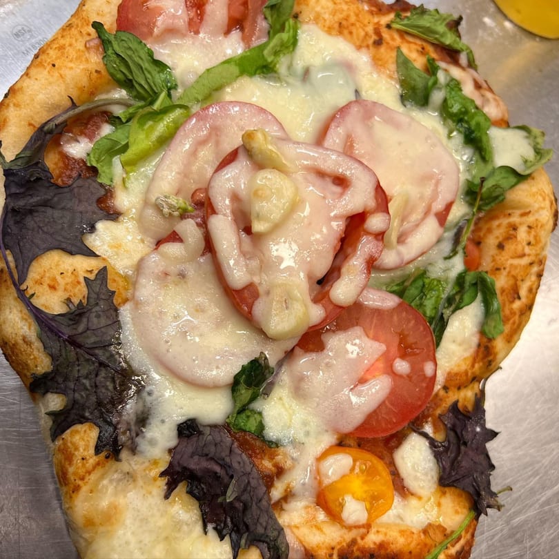 Close-up of a pizza with melted cheese, sliced tomatoes, and green and dark leafy greens.